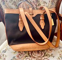 Front view of black canvas bucket bag with tan leather base and straps