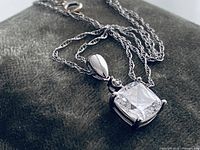 Pendant and chain close-up on dark fabric, showing gemstone, bail, chain and clasp