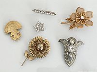 All six brooches laid out showing variety of designs and metals