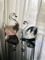 Both swan figurines side by side on reflective surface