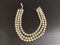 Full view of signed Marvella three-strand faux pearl necklace laid flat