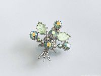 Front view of silver-tone brooch showing five aurora borealis rhinestones and two green glass leaves