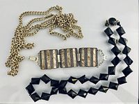 All three jewellery pieces laid out: gold chain necklace, marbled lucite panel bracelet, black bead necklace