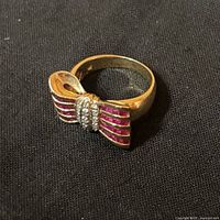 14K gold bow ring with pink sapphire inlays and diamond center displayed on dark fabric