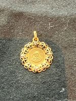 Front view of round yellow gold pendant with Virgin Mary relief and filigree edge