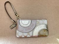 Front view of Coach metallic patchwork wristlet with wrist strap and hangtag visible