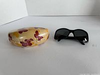 Sunglasses and floral hard case displayed on white surface
