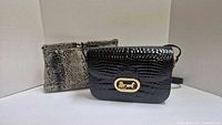 Front view of both bags showing black crocodile-embossed Valerie Jean bag with gold plaque and tan/cream snake-print bag
