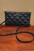 Front view of black quilted Kate Spade crossbody clutch showing gold-tone hardware and strap