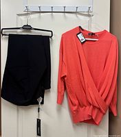 Coral wrap sweater and black dress pants displayed on hangers with tags visible