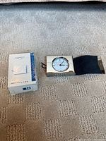 Clock, sleeve, and box side-by-side on carpet