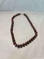 Full view of the single-strand reddish-brown pearl necklace laid flat in oval form
