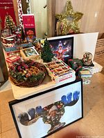 Overall view of assorted Christmas décor on table including ceramic tree, ornaments, framed puzzles, basket and topper