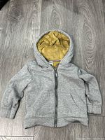 Front view of gray hoodie laying flat showing zipper and pockets