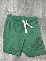 Front view of green terry shorts showing drawstring and dinosaur skateboard graphic