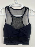Front view of black mesh and solid sleeveless crop top on hanger