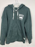 Front view of green Roots full-zip hoodie on hanger showing overall design
