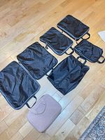 All seven black packing cubes and one pink toiletry bag displayed on floor