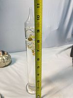 Full height view of Galileo thermometer beside tape measure showing approximately 11 inches