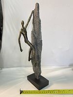 Full view of sculpture showing climber figure, rock form, and base