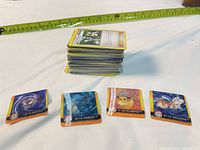 Stack of Pokémon TCG cards with four square character cards in foreground and measuring tape for scale