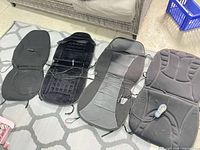 Four black car seat pads laid out to show variety and cables