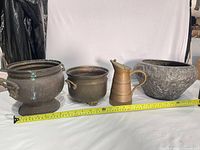 Group view of four metal vessels with measuring tape for scale