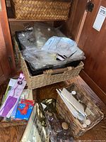 Overview of baskets inside cabinet showing large seagrass basket with photo sleeves, small wicker basket with pads, ribbons and game packs