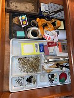 Drawer with compartment tray showing safety pins, clips, pushpins, dowels, crochet hook, scissors, labels, tape and organizer trays