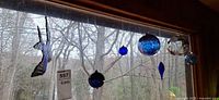 Wide view of stained glass hummingbird with multiple blown glass ornaments hanging on window