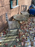Round wooden table and two wooden chairs on deck, showing overall condition