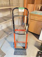 Front view of orange and black steel hand dolly showing handle, frame, wheels and toe plate