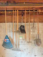 Overall view of seven long-handled garden tools hanging on rack