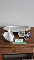 Lot overview showing platter, swan figurine, three alarm clocks on table