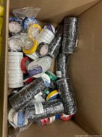Open box showing numerous shrink-wrapped packs and loose rolls of electrical tape