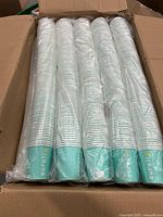 Four sealed sleeves of teal-striped paper cups in open box