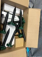 Top view of box showing multiple black pest repeller stakes with green heads and inner cartons