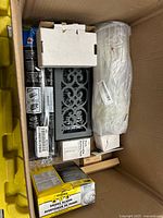 Top view inside box showing decorative vent cover, white wrapped item, long packaged wiper blade, smoke alarm box