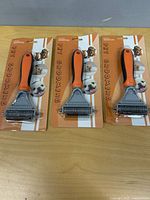 Three packaged pet grooming deshedding brushes on table