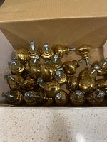 Open box showing bulk of brass-tone cabinet knobs with screws attached