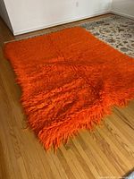 Full view of orange Flokati rug on wood floor showing size and color