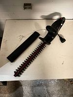 Hedge trimmer with blade cover beside it, showing full length of 16 in blade