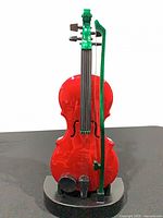 Front view of red electronic violin with green bow on black stand