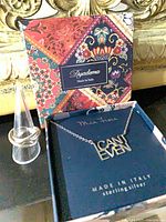 Necklace in original Mia Fiore box with ring on display cone beside Dyadema box