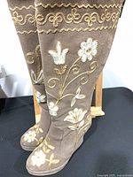 Full view of both knee-high suede boots on stand