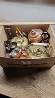 Overall lot in box showing kettles, creamer, bud vase, goblet and small metal items