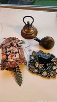 Group shot showing all four items: clock, brass bell, ceramic bird figurine, glazed tile