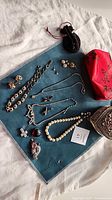 Assortment spread on blue mat showing necklaces, bracelet, brooch, pendants, earrings, pouches and cases