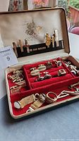 Open jewelry box showing cufflinks, tie bars and other accessories in red velvet tray