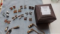 Overview of cufflinks, tie clips, chain guard, and Penney’s box on cloth